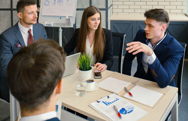Brainstorm. Group of business people looking at the laptop together. One business woman looking at camera