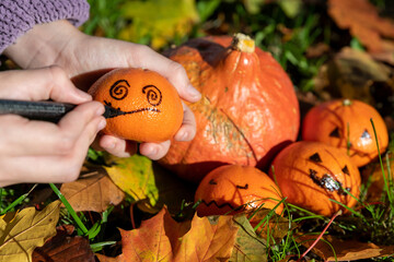 Kindliche Hände basteln Halloween Deko im herbstlichen Garten mit Clementinen, Kürbis und bunten Blättern.