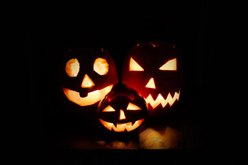 Three Jack-o'-lantern pumpkins near burning fireplace in the dark