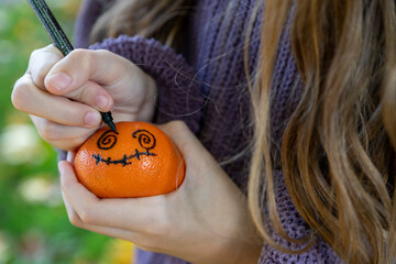 Ein Mädchen bemalt Clementinen für ein Halloween Deko. Nahaufnahme Kinderhände mit einem...
