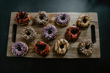 conjunto de donuts de diferentes colores con chocolate y azúcar encima de una tabla de madera