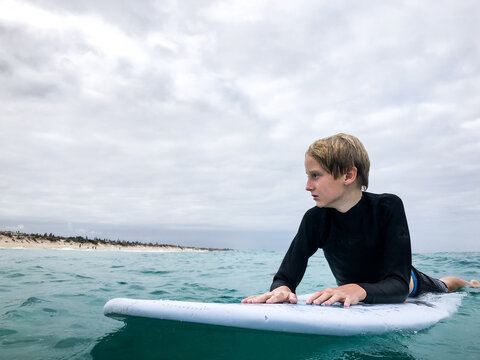 Male youth sitting on boogie board waiting for waves on overcast day