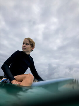 Male youth sitting on boogie board waiting for waves on overcast day