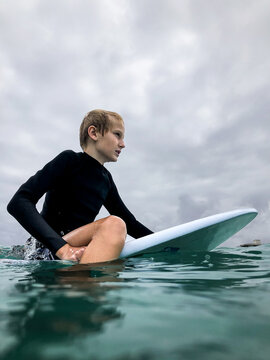 Male youth sitting on boogie board waiting for waves on overcast day