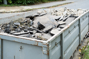 Big Overloaded dumpster waste container filled with pieces of removed asphalt, construction waste near a road digging construction site. - obrazy, fototapety, plakaty