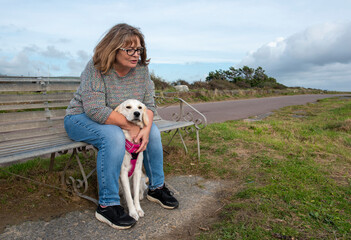 Upset and depressed mature female owner sitting on park bench with golden retriever dog 