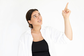 Portrait of happy young woman pointing upwards and smiling. Caucasian lady wearing black top and white T-shirt showing something against white background. Advertising concept