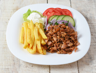Doner kebab or gyros. Chicken meat on a white plate with salad and french fries. Copy space for text. Wooden background	