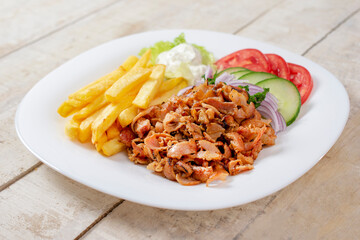 Doner kebab or gyros. Chicken meat on a white plate with salad and french fries. Copy space for text. Wooden background
