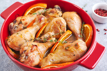 Chicken drumsticks with oranges and thyme baked in red round baking dish