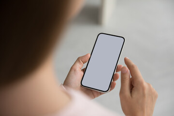 Unknown woman holds mart phone with white blank mock up screen view, close up. Female using web site, makes call, order goods, enjoy remote comfort services, advertising new application or software
