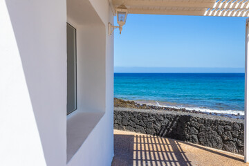 Fototapeta na wymiar Seascape from the window. White house with a pergola and big sea view windows. Perspective lines leading to the blue sea. Summer vacations beach house. There is copy space for design.