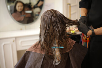 女性の髪に薬剤を塗布する男性美容師