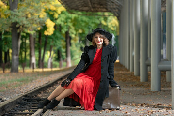 Woman with retro suitcase at train station waiting for train. Style 30-40s.Girl in vintage clothes in autumn on platform