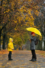 Mom and child are standing in rain in autumn park. Walking in rainy weather. Vertical frame