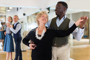 Elderly woman learning ballroom dancing in pair in dance studio
