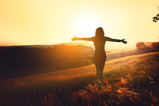 Happy standing woman looks at the sunset with open hands.