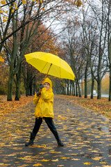 Little boy walks in the park and plays with an yellow umbrella. Walking with child in rain. Vertical frame