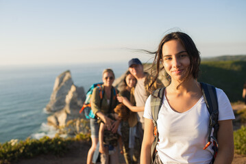 Portrait of smiling teen girl posing on mountain with her family in background. Happy teenager hiking with family in summer. Adolescence and family weekend concept