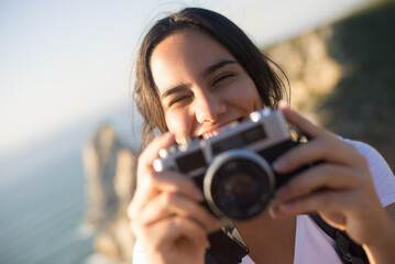 Close-up of smiling teen girl holding camera. Portrait of happy young photographer outdoors. Travel...