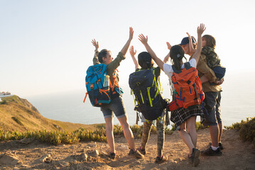 Rear view of happy hiking family raising arms on mountain. Excited parents traveling with children outdoors. Active family concept