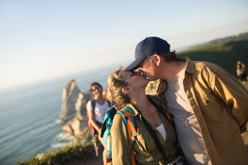Happy mid adult couple kissing on top of mountain. Portrait of loving backpackers with children in background. Active family and relationships concept