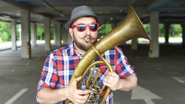 A street musician wearing sunglasses plays the tuba outside.