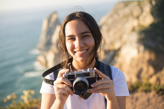 Portrait of teenage girl with camera smiling. Attractive young girl travelling in mountains. Travel and hiking concept