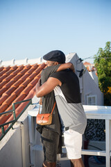 Side view of African gay couple hugging on roof top in summer. Two happy men in casual clothes standing embracing enjoying date. Same sex couples private life, choice, love and happy relations concept