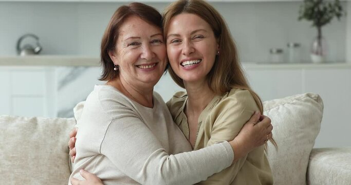 Young and older women embracing seated on sofa at home. Happy grown up daughter cuddling senior mom feeling unconditional love, express protection and caress, enjoy time together. Family ties concept
