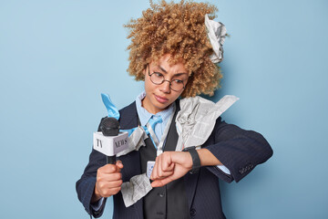 Busy female reporter or journalist holds microphone looks at smartwatch checks time waits for...