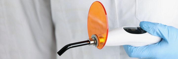 The doctor is holding dental led curing light, close-up