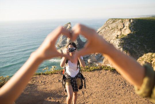 Teenage girl taking photo of heart shape gesture in mountains. Portrait of young photographer with camera hiking in summer. Travel and hiking concept