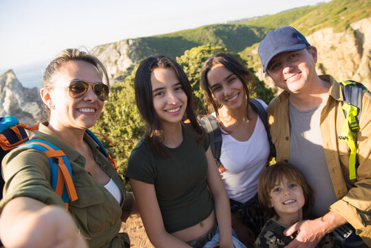 Selfie of family looking and smiling in mountains. Portrait of happy parents with daughters and son hiking in summer. Active family weekend concept