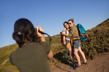 Girl taking photo of hiking woman with daughter. Mother embracing teen girl and posing outdoors in summer. Active family weekend concept