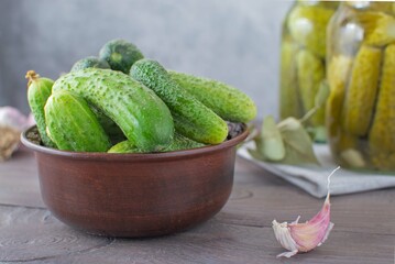 Fresh green cucumbers in a clay bowl and pickled cucumbers in a glass jar. Selective focus.