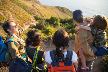 Hiking mid adult woman showing view to her family. Rear view of parents and children standing at precipice when travelling. Active family concept