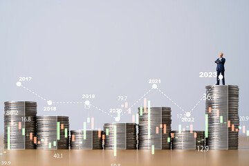 Businessman standing on top of coins stacking with stock market graph chart and business year for...