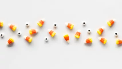 Foto op Canvas A line of candy corn and candy eyeballs, against a white background. © Carey