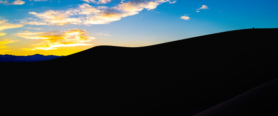 Mesquite Flat Sand Dunes and abstract geometry of curving silhouette desert hills at sunset in Death Valley National Park, California