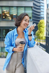 Outdoor shot of Asian woman wears big transparent eyeglasses blue shirt smartwatch sends voice...