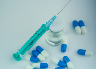 Syringe injecting liquid into a vial, with capsules in the foreground. Medical and healthcare...