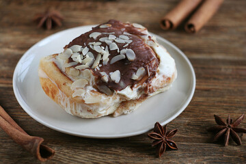 Brioche bun lies in a plate on a wooden table. Nearby are cinnamon sticks and star anise.