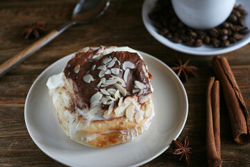 Brioche bun lies in a plate on a wooden table. Nearby are cinnamon sticks and star anise.
