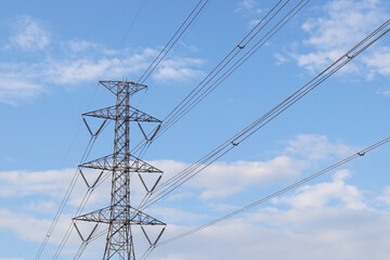 High-voltage electricity transmission tower with multiple power lines against a bright blue sky and scattered clouds, symbolizing energy infrastructure, sustainable power distribution