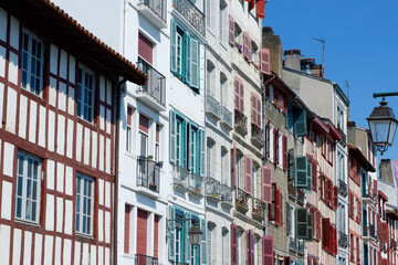 Fototapeta na wymiar Colourful vintage facades of typical french basque homes with shutters and windows of faded colours downtown in Bayonne, Basque country, Spain