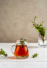 Thyme honey in small jug , thyme branch on white wooden table with grey background
