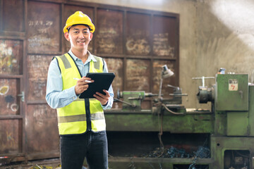 Portrait of industrial worker indoors in factory. Work at the Heavy Industry Manufacturing Factory. Manual workers discussing while using smart phone at factory. Smiling and happy employee.