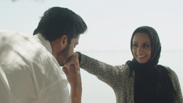 Handsome muslim man kissing hand of smiling lady in hijab. Close-up of dark-haired Arabian guy expressing feelings to his woman while spending time together outside. Courtship, ethnicity concept.