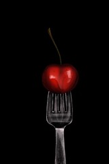 cherry on a fork on a black background vertical